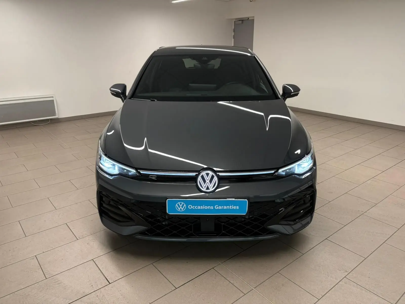 Vue frontale d'une Volkswagen Golf 1.5 eTSI 150 DSG7 R-Line Edition en gris dauphin avec phares LED allumés en intérieur.
