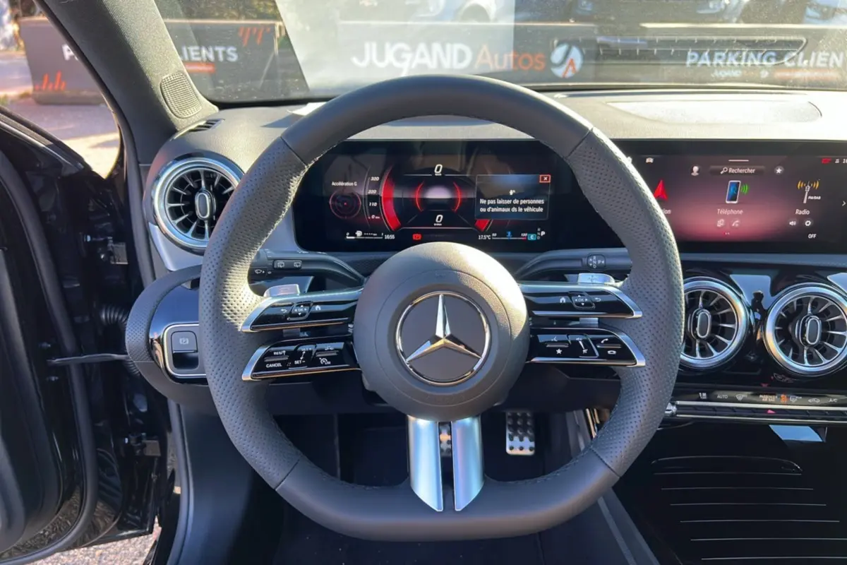 Vue centrée sur le volant cuir perforé et le tableau de bord numérique d'une Mercedes Classe A noire cosmos, intérieur moderne et lumineux.