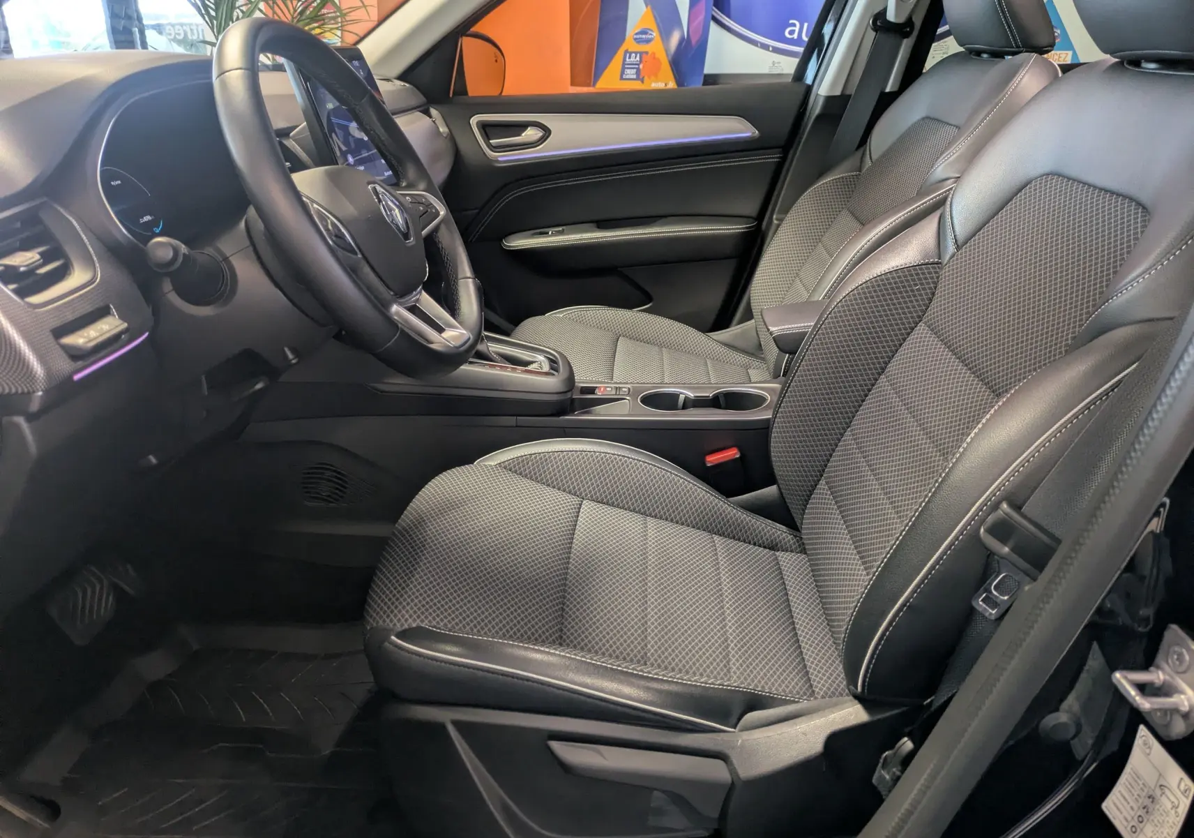 Vue intérieure côté conducteur du Renault Arkana 2023 noir, mettant en valeur les sièges en tissu et cuir avec console centrale et volant multifonction.