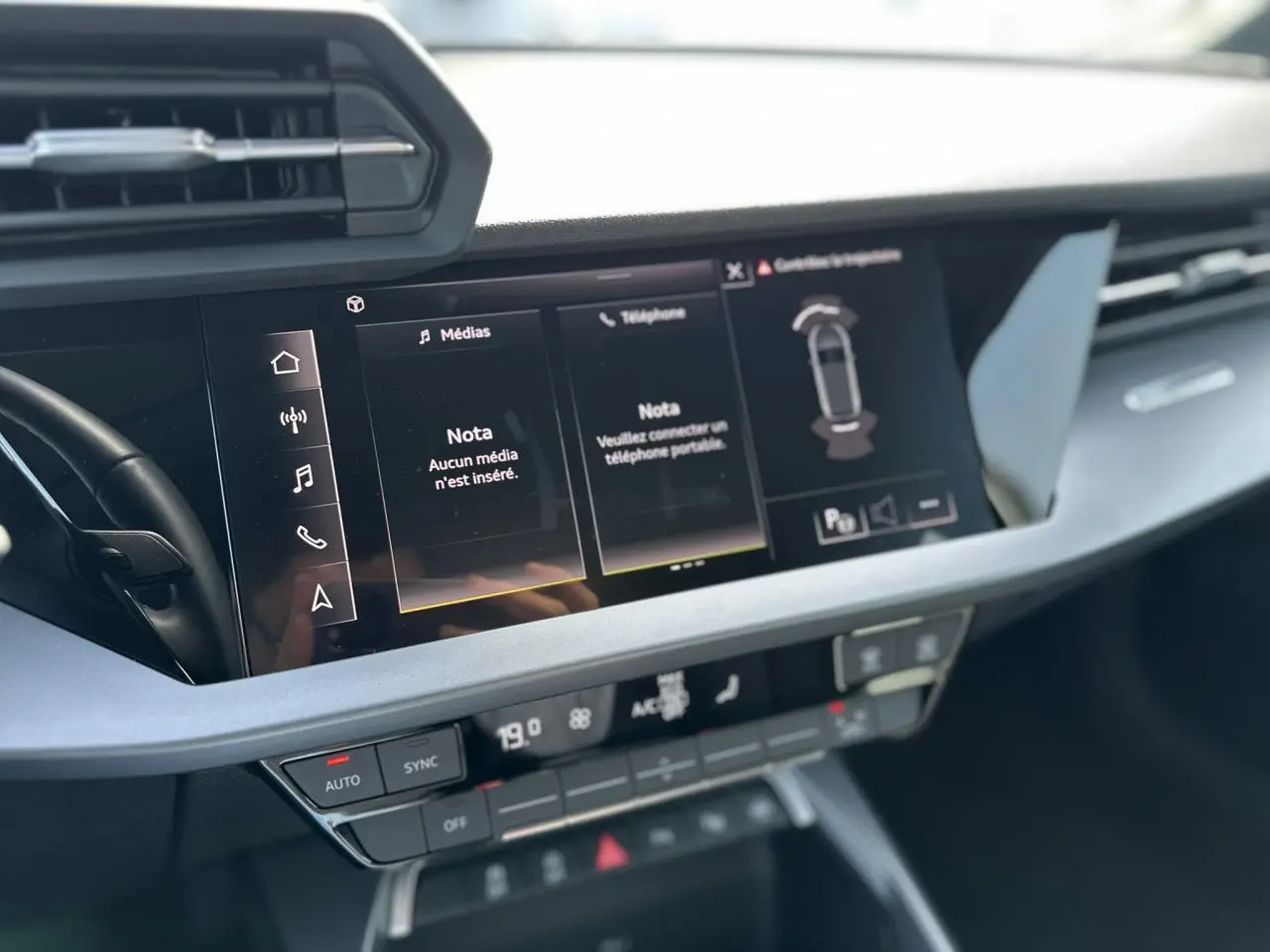 Vue rapprochée de la console centrale de l'Audi A3 Sportback 2024 blanche, affichant l'écran tactile multimédia et les commandes climatiques.