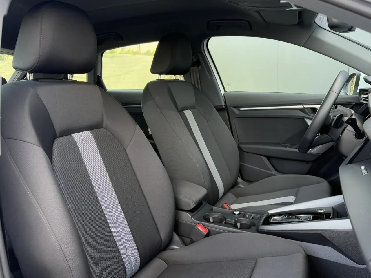 Vue intérieure côté droit de l'Audi A3 Sportback 2024 avec sièges tissu Konsens gris foncé et console centrale moderne.