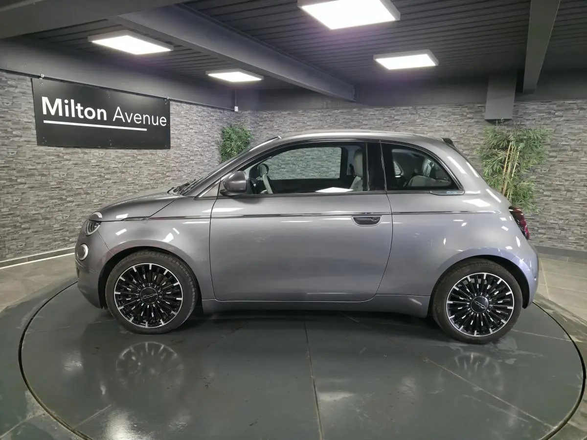 Profil droit d'une FIAT 500 Cabriolet électrique gris foncé avec jantes alliage bicolores en showroom.