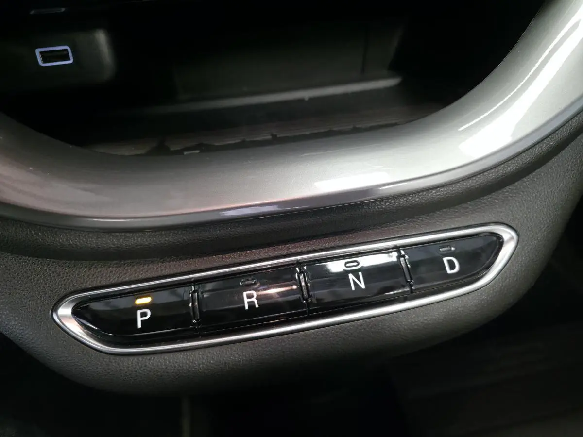 Gros plan sur la commande de boîte automatique noire avec éclairage orange sur la position P dans une Fiat 500 Cabriolet électrique gris foncé.