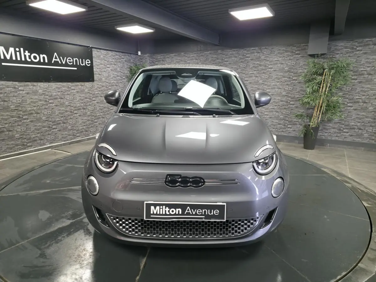 Vue frontale d'une FIAT 500 Cabriolet électrique gris foncé avec logo 500 noir et calandre épurée en intérieur showroom.