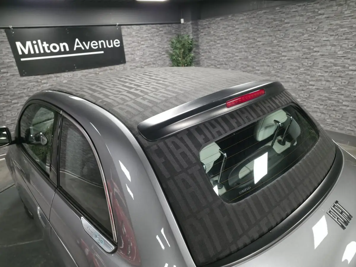 Vue arrière côté gauche d'une FIAT 500 Cabriolet électrique gris foncé avec capote à motif FIAT visible.
