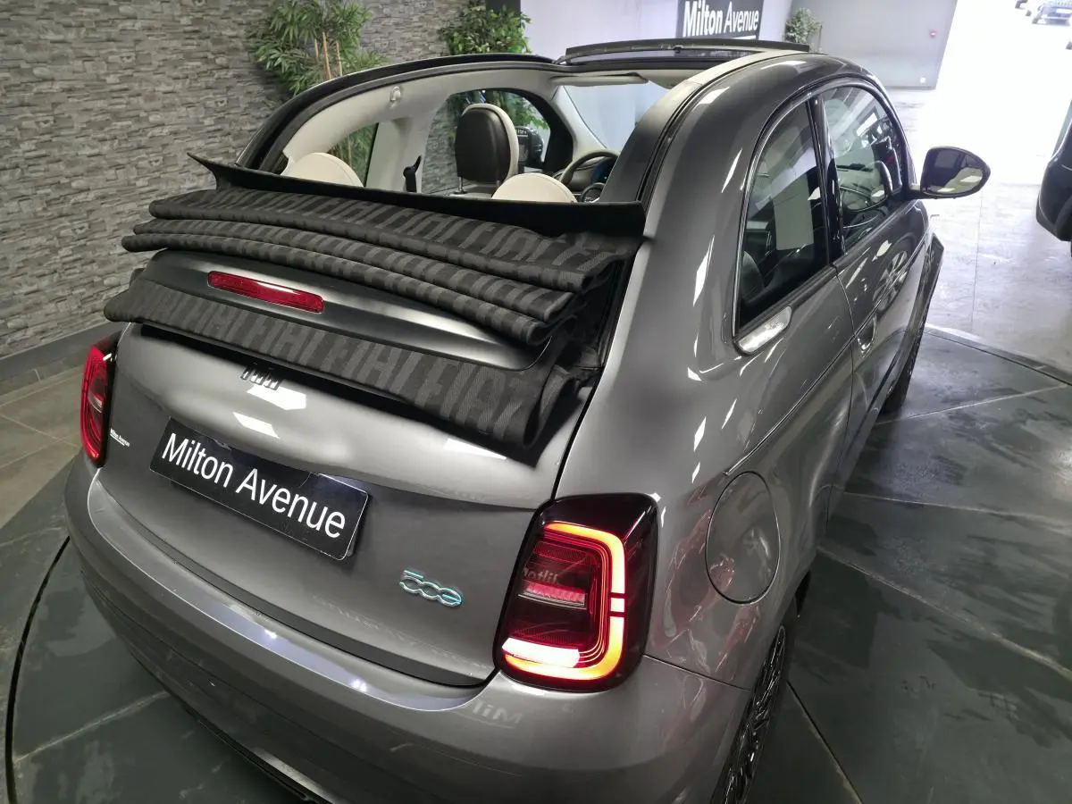 Vue 3/4 arrière droite d'une FIAT 500 Cabriolet électrique gris foncé avec capote partiellement ouverte et feux arrière allumés.