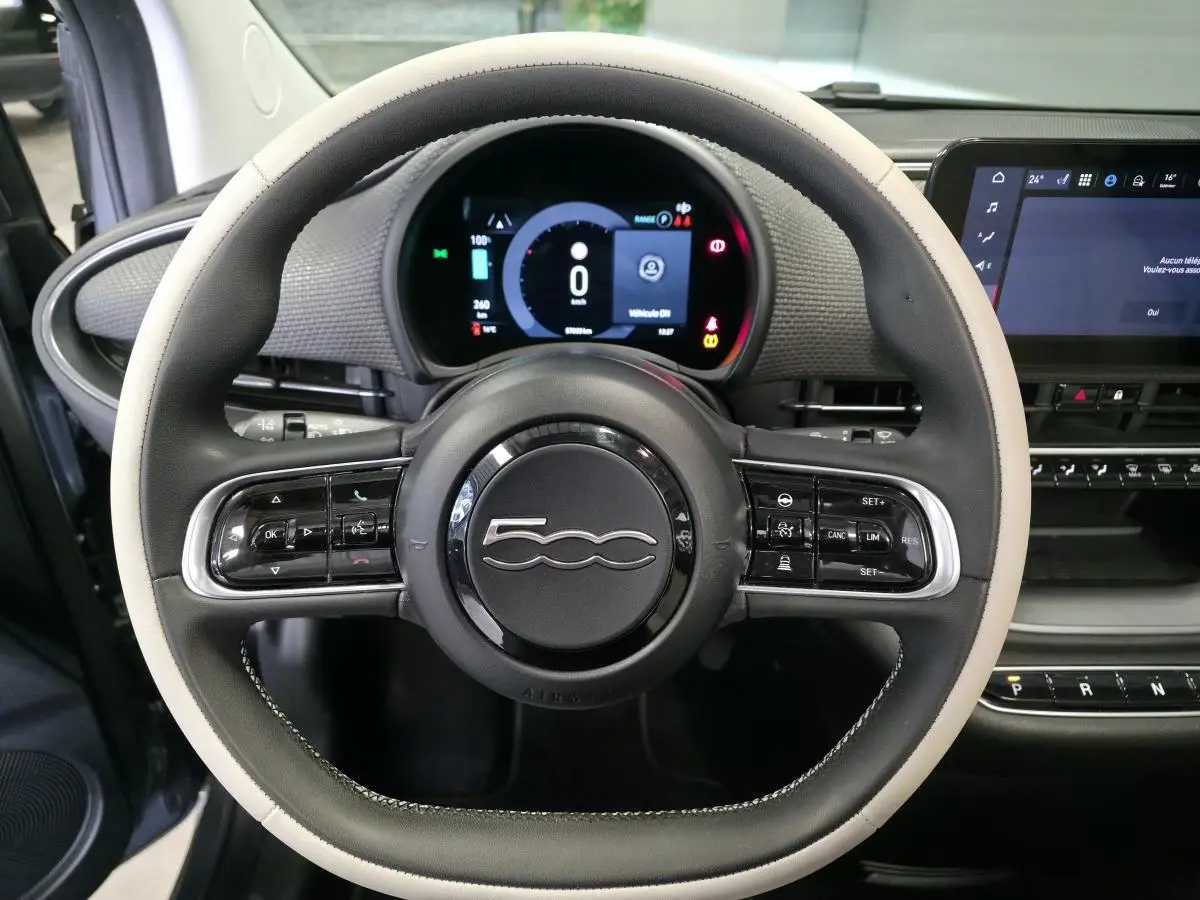 Vue rapprochée du volant bicolore noir et beige avec logo 500, tableau de bord numérique et écran tactile de la Fiat 500 Cabriolet électrique.
