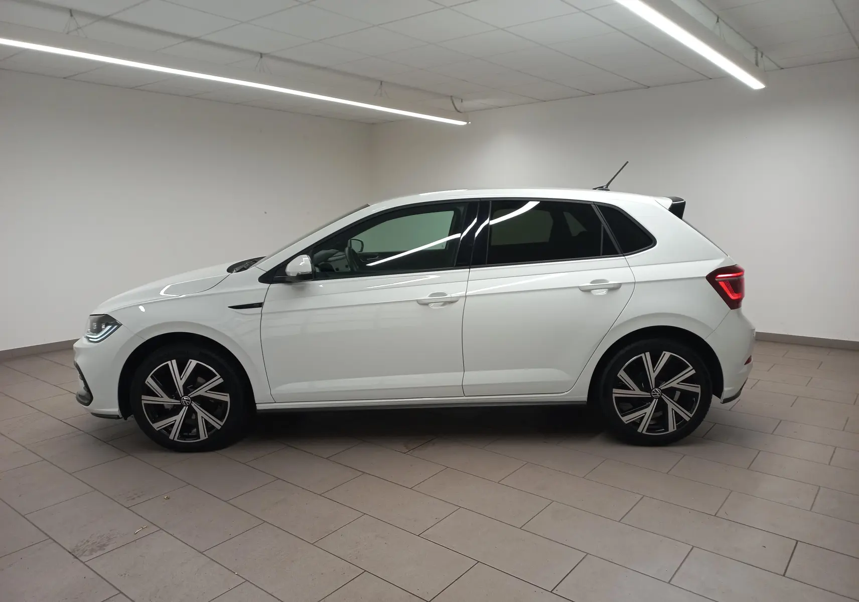 Vue de profil côté gauche d'une Volkswagen Polo blanche avec vitres arrière surteintées et jantes R-Line distinctives.