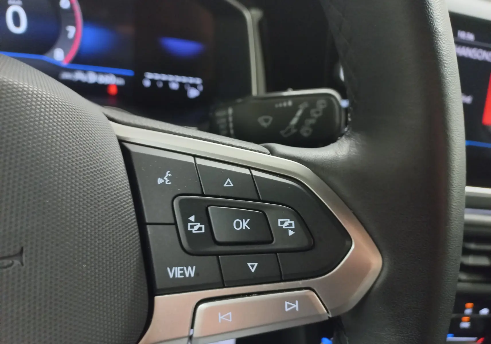 Gros plan sur les commandes multifonctions du volant noir de la Volkswagen Polo 2025, avec écran numérique en arrière-plan.