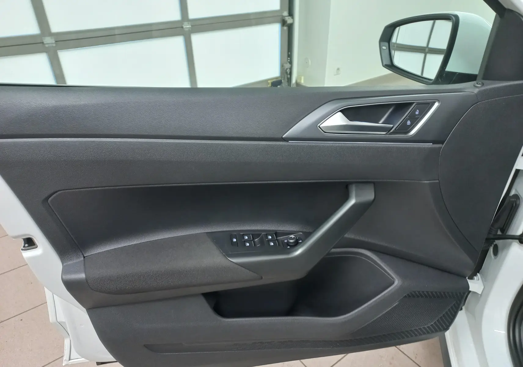 Vue intérieure côté gauche de la porte avant d'une Volkswagen Polo blanche avec commandes de vitres et verrouillage.