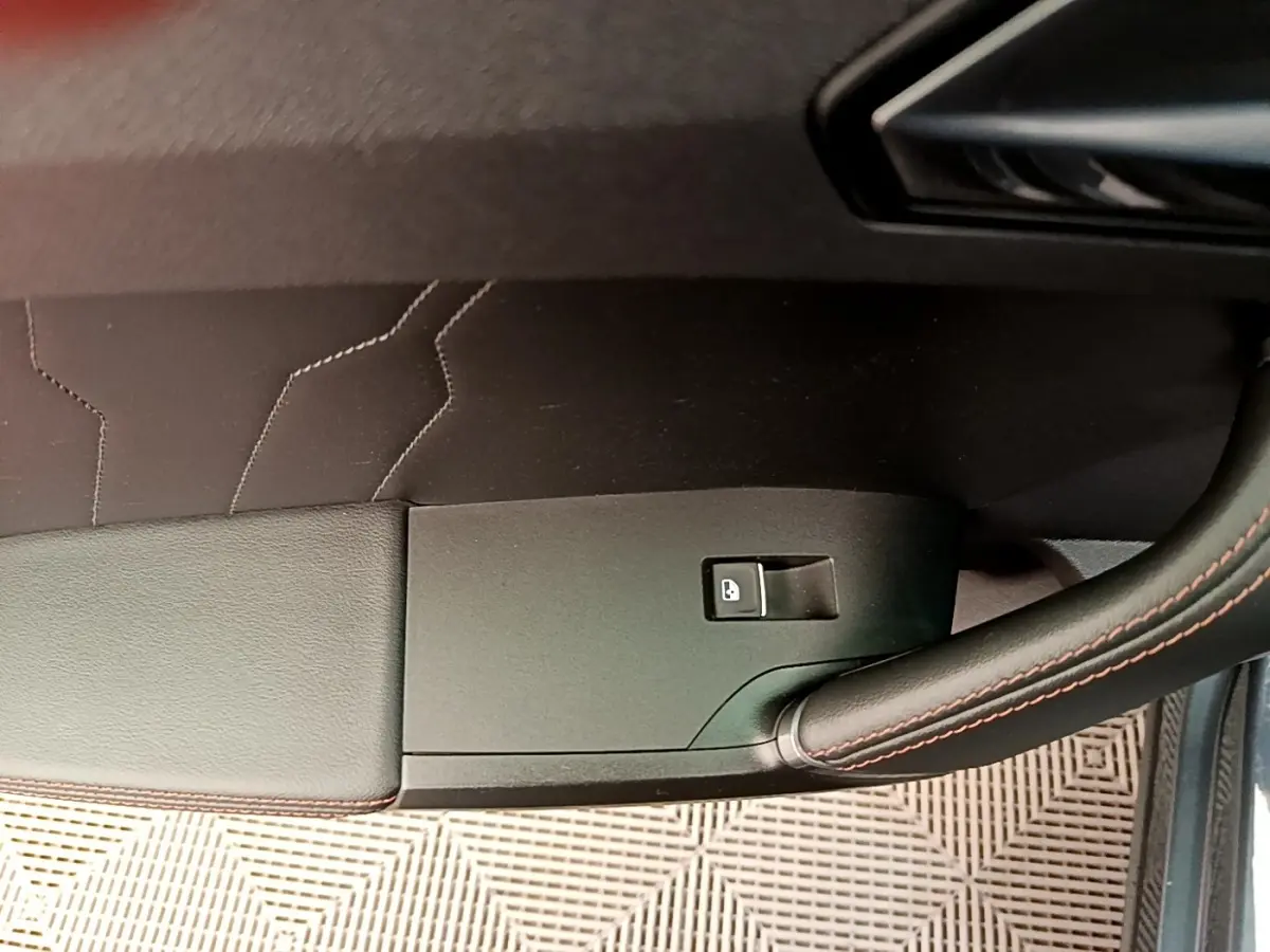 Détail de la porte côté conducteur d’une CUPRA Formentor gris foncé, avec bouton de verrouillage et surpiqûres rouges.