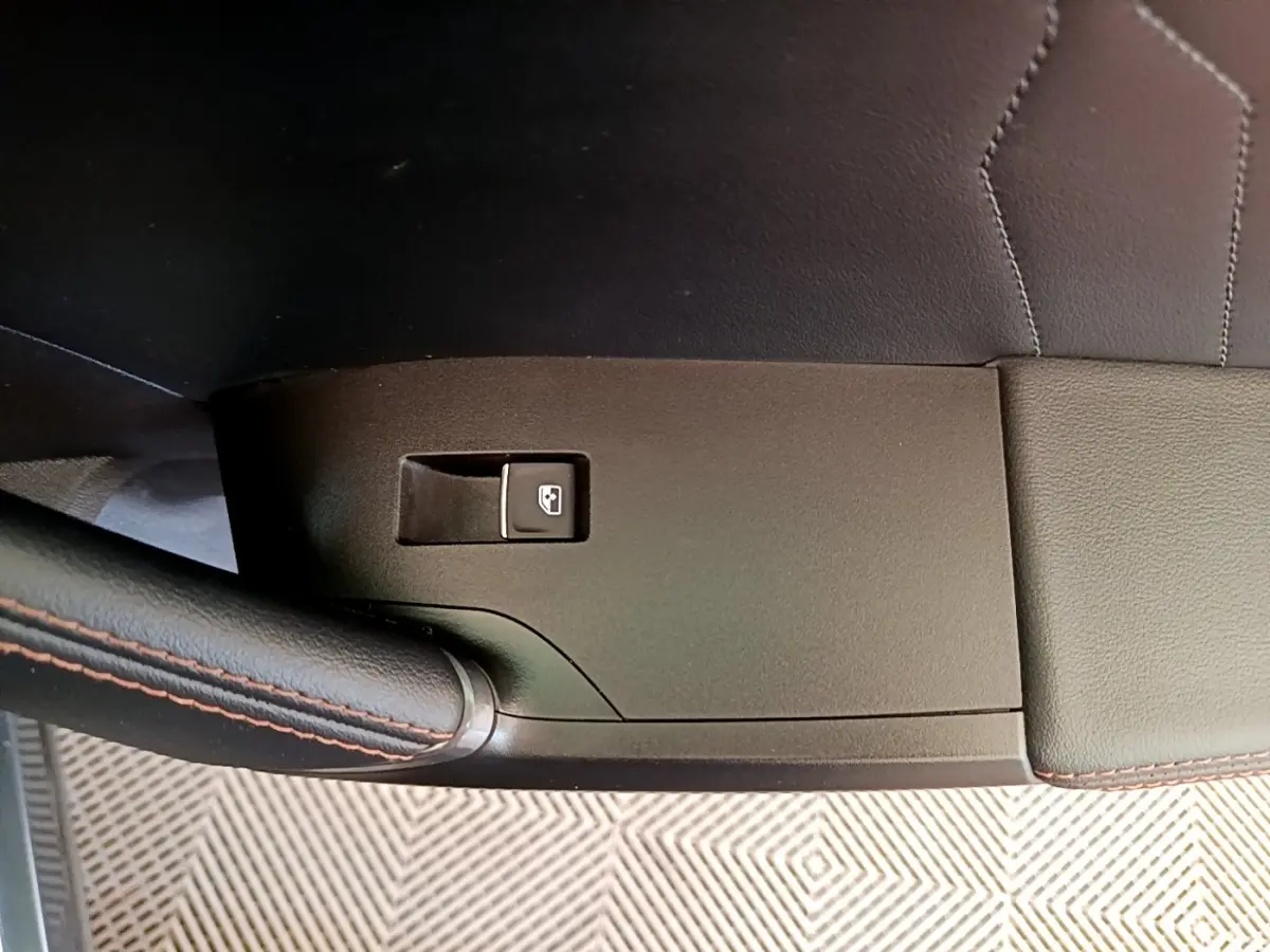 Gros plan sur la commande de lève-vitre côté conducteur avec surpiqûres orange sur cuir noir.