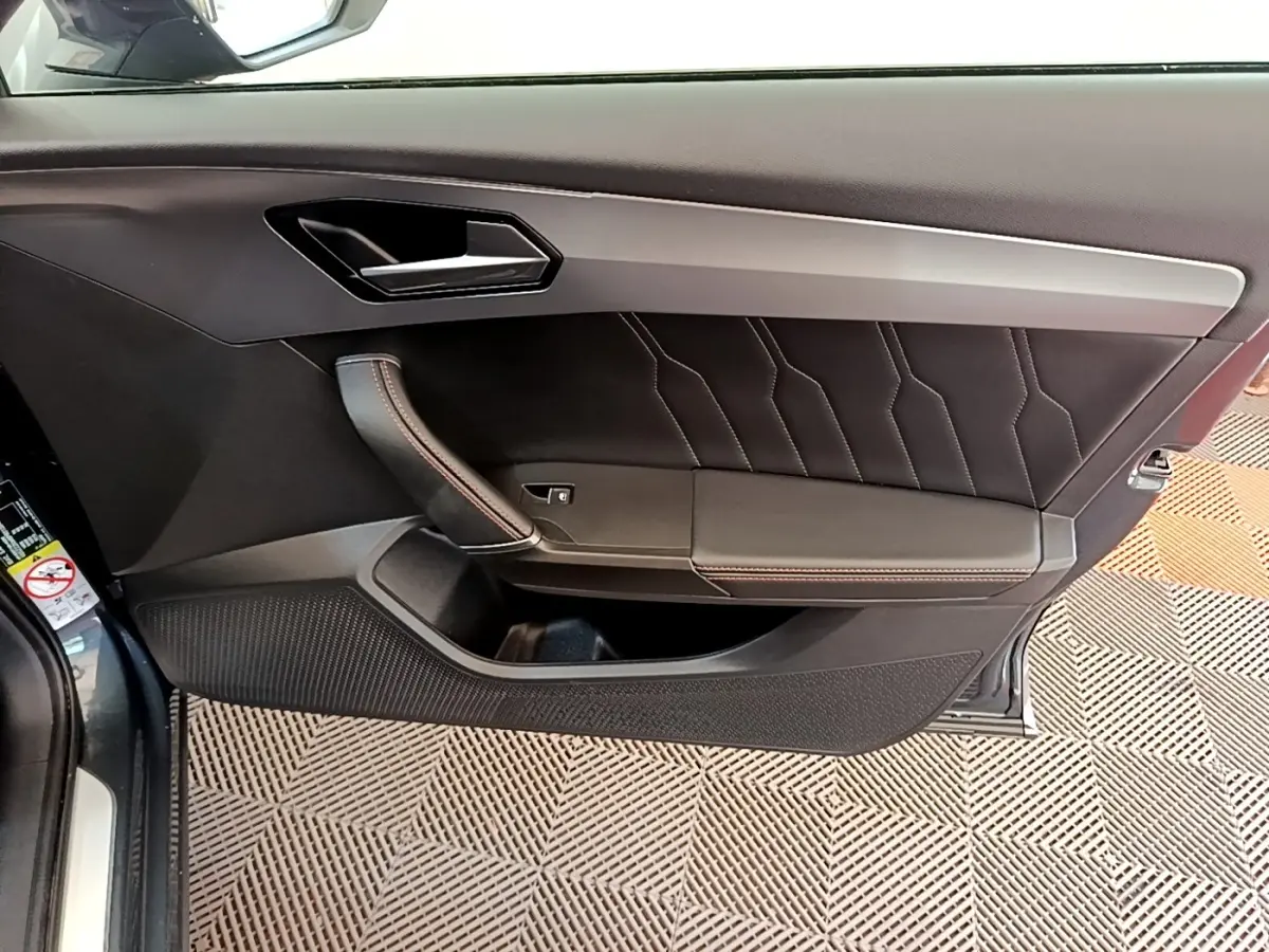 Vue intérieure côté gauche de la porte d’une CUPRA Formentor gris foncé avec garniture cuir et surpiqûres rouges.