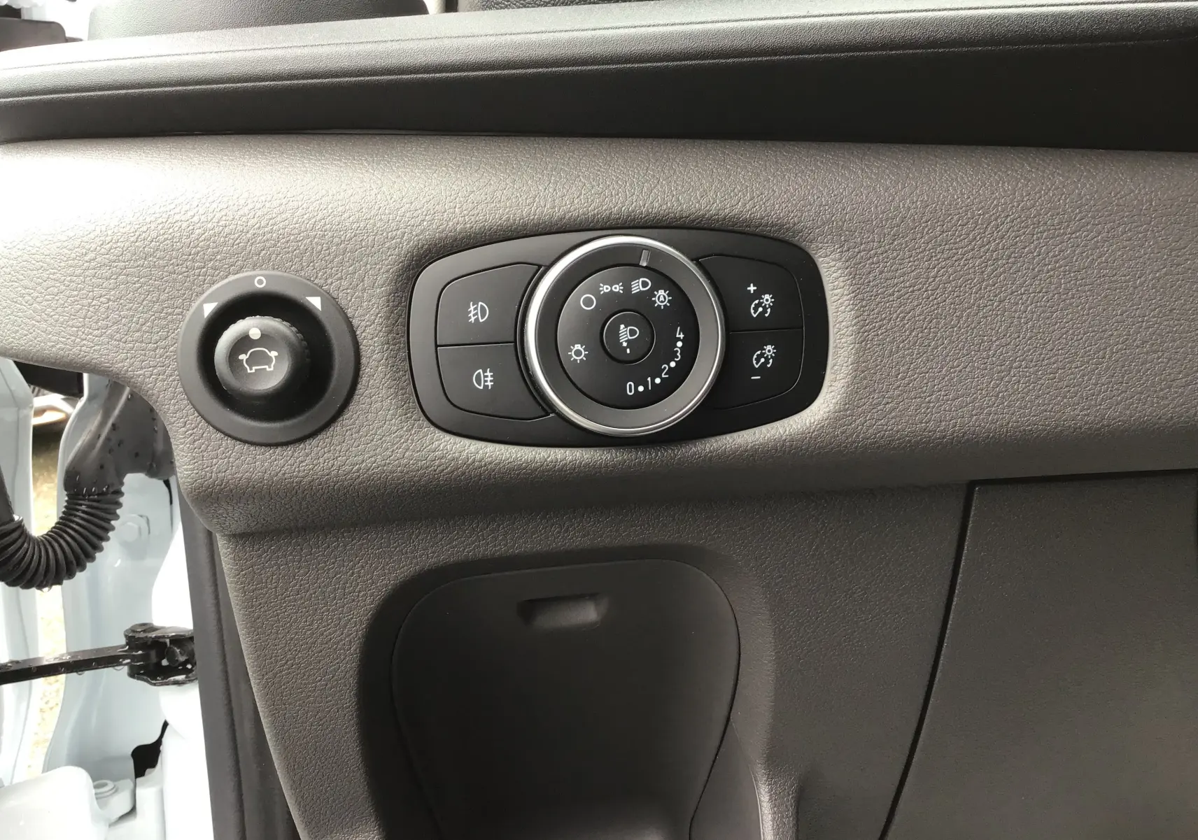 Gros plan sur les commandes d'éclairage et réglage des phares du Ford Transit Fourgon blanc, côté gauche du tableau de bord.