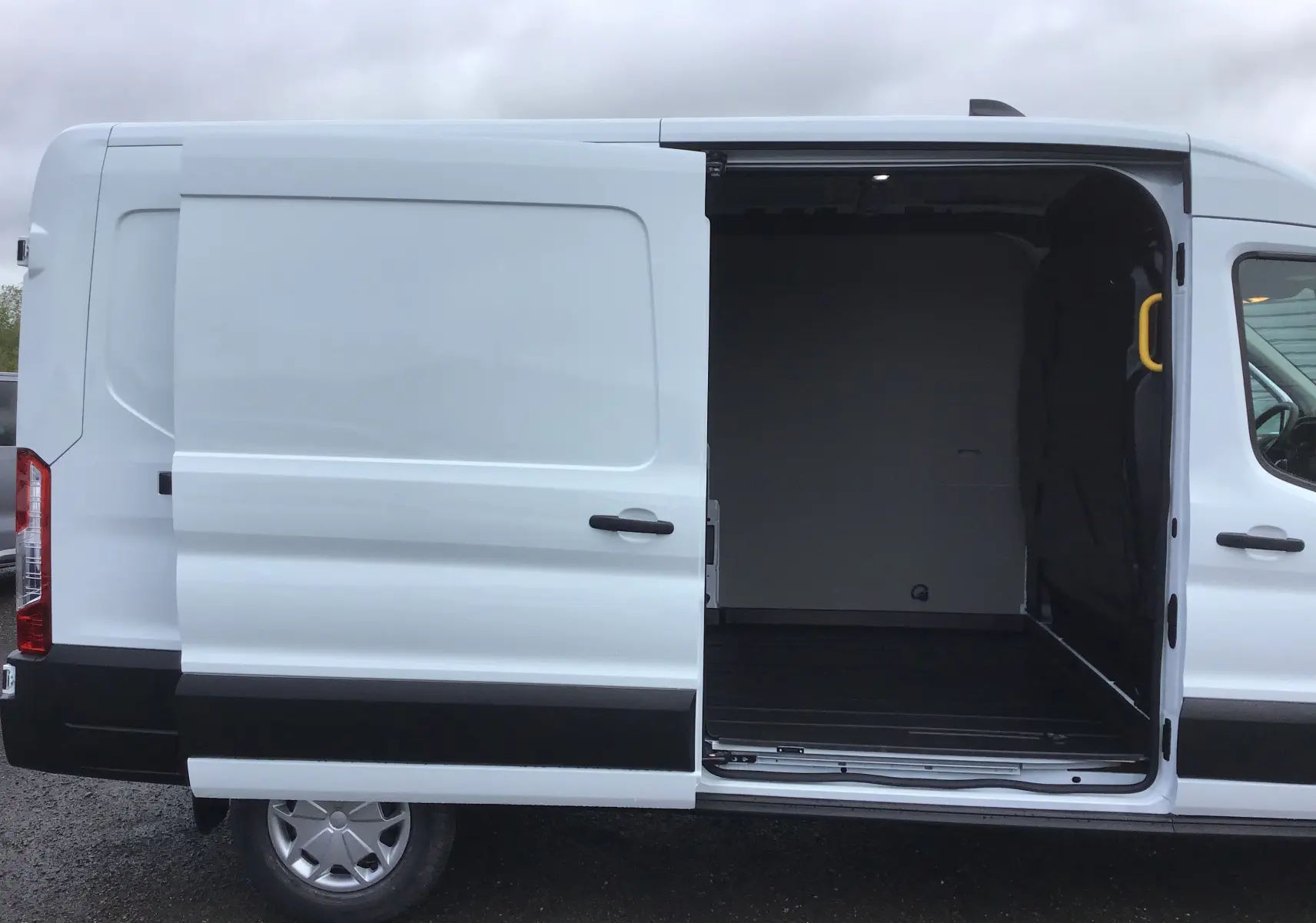 Vue latérale gauche d'un fourgon Ford Transit blanc avec la porte coulissante ouverte montrant l'espace de chargement vide.