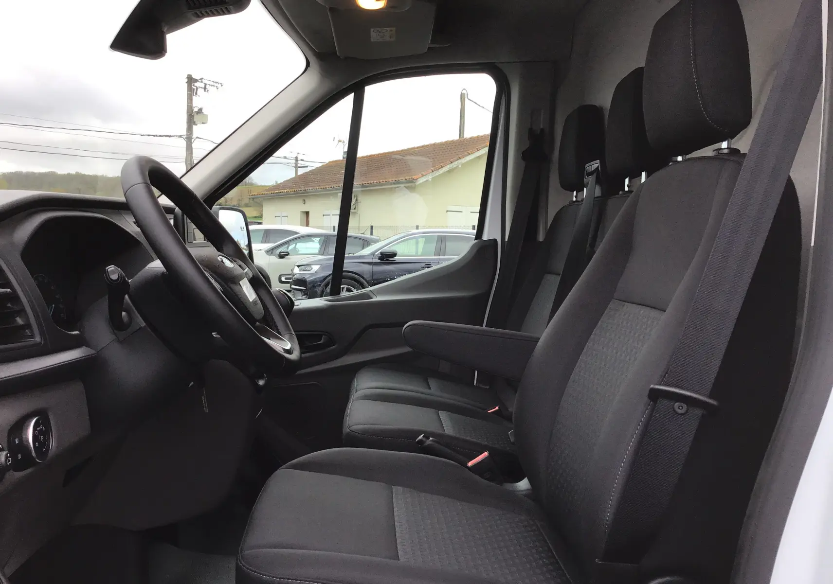Vue intérieure côté conducteur du Ford Transit Fourgon blanc 2023, montrant les sièges noirs et le volant.