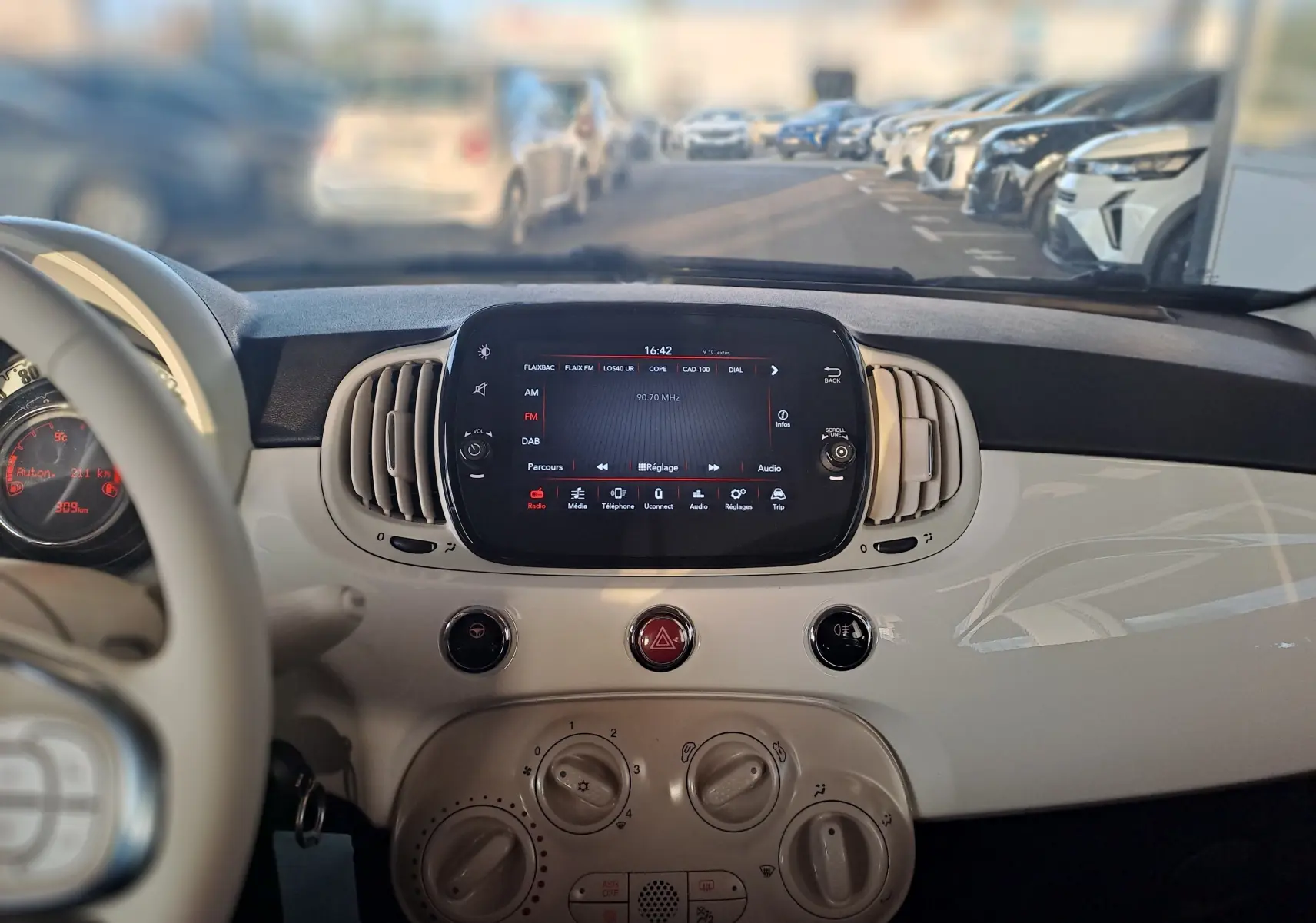 Tableau de bord blanc de la Fiat 500 2023 avec écran tactile central et commandes de climatisation en vue frontale intérieure.