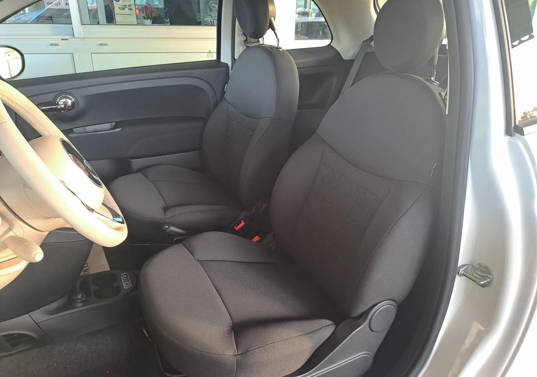 Vue intérieure côté gauche montrant les sièges noirs et le volant beige d'une FIAT 500 blanche 2023.