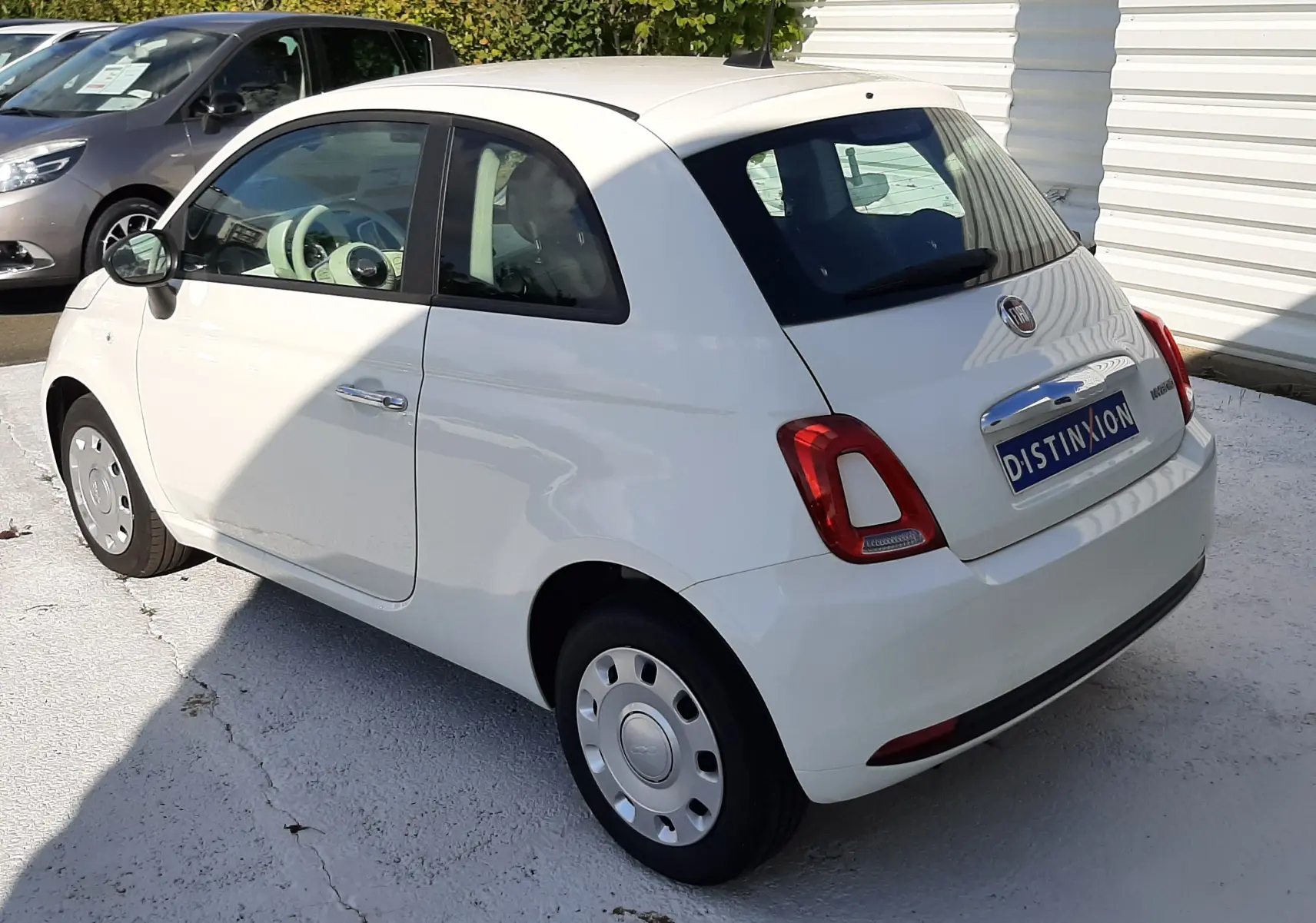 Vue 3/4 arrière droite d'une Fiat 500 blanche 2023 avec jantes acier et logo Distinxion sur le coffre.