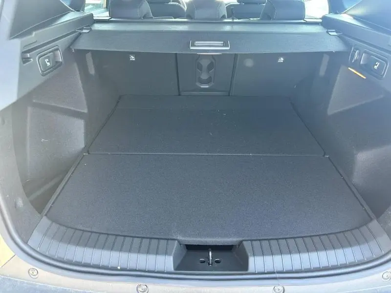 Coffre spacieux du Dacia Bigster blanc, vue de l'arrière avec banquette rabattue et cache-bagages déployé.