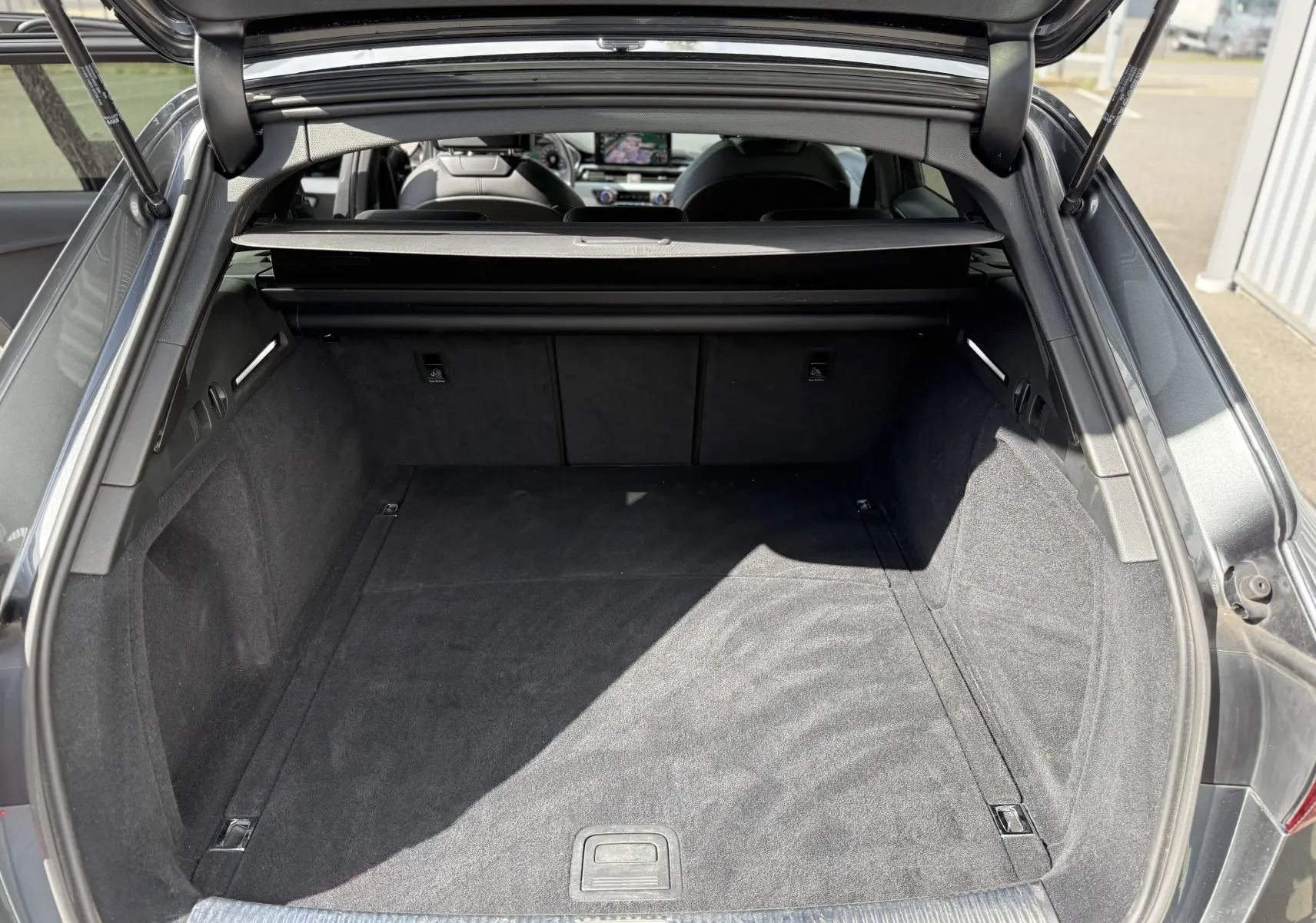 Coffre ouvert vu de l'arrière d'une Audi A4 Avant 35 TDI gris Daytona metal, intérieur noir et espace de chargement spacieux.