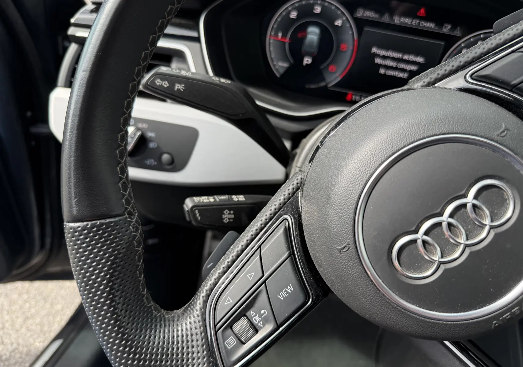 Gros plan sur le volant en cuir noir perforé et le tableau de bord numérique de l'Audi A4 Avant gris Daytona 2023.