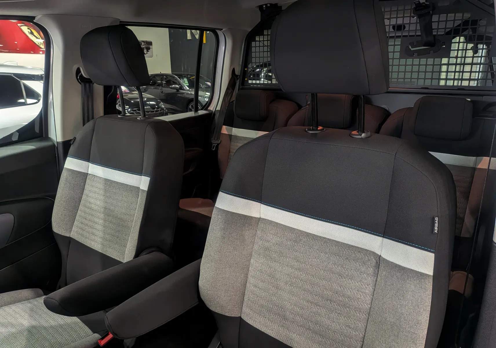 Gros plan sur les sièges avant en tissu gris et noir du Citroën Berlingo Blanc Glacier, version utilitaire avec séparation grillagée.