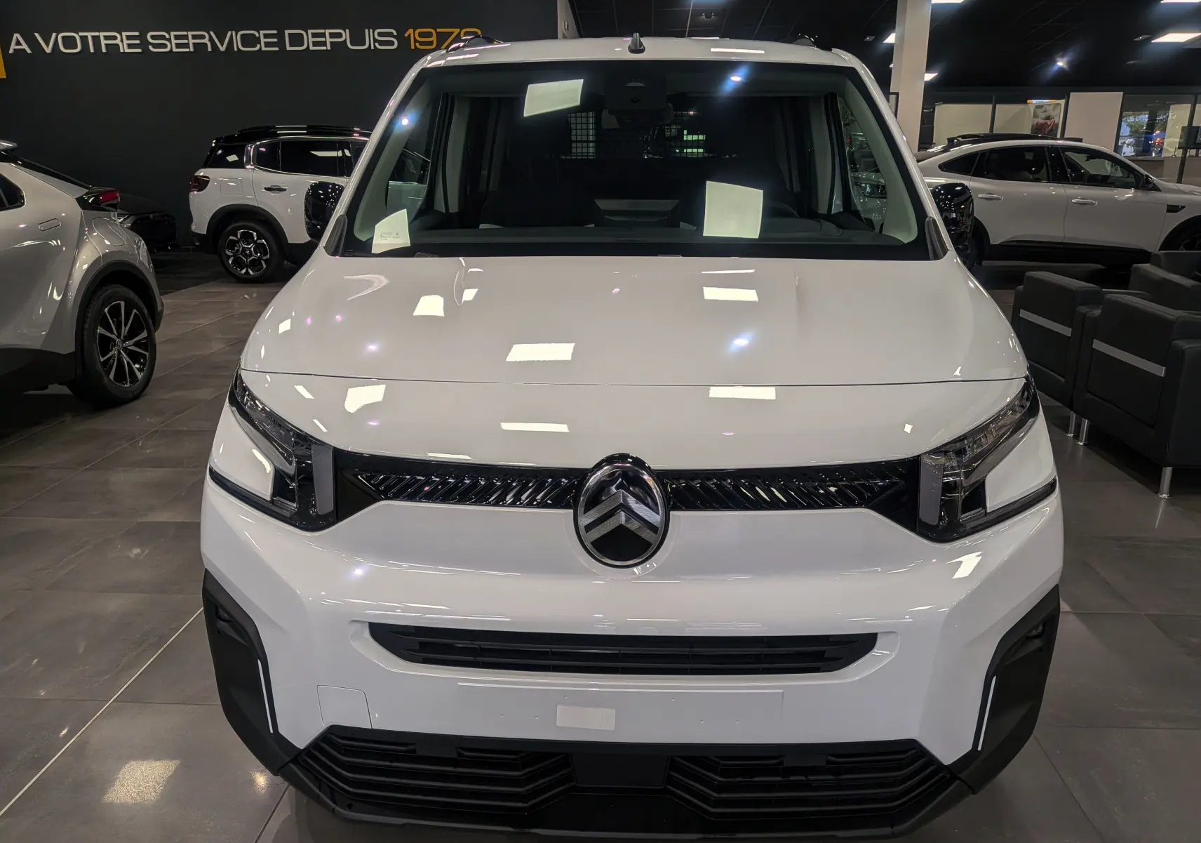 Vue frontale d'un Citroën Berlingo 2025 blanc glacier en showroom, soulignant sa calandre noire et ses phares modernes.