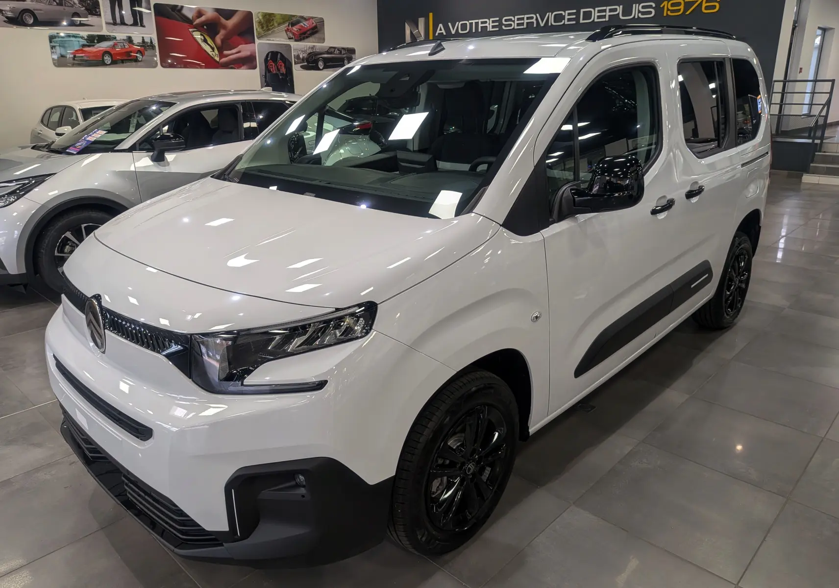 Vue 3/4 avant droite d'un Citroën Berlingo Blanc Glacier avec jantes noires et protections latérales noires.