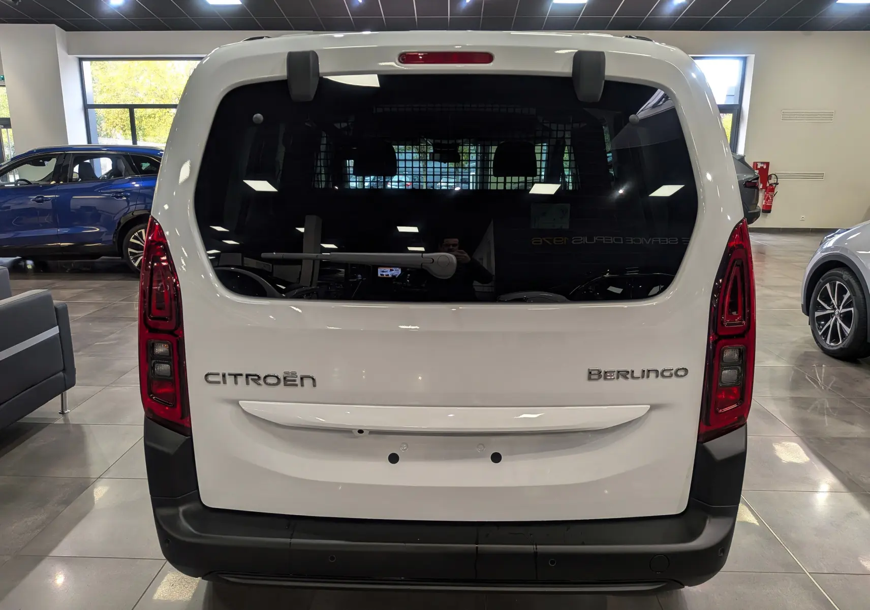 Vue arrière d'un Citroën Berlingo blanc glacier en showroom, avec vitres teintées et feux verticaux rouges.