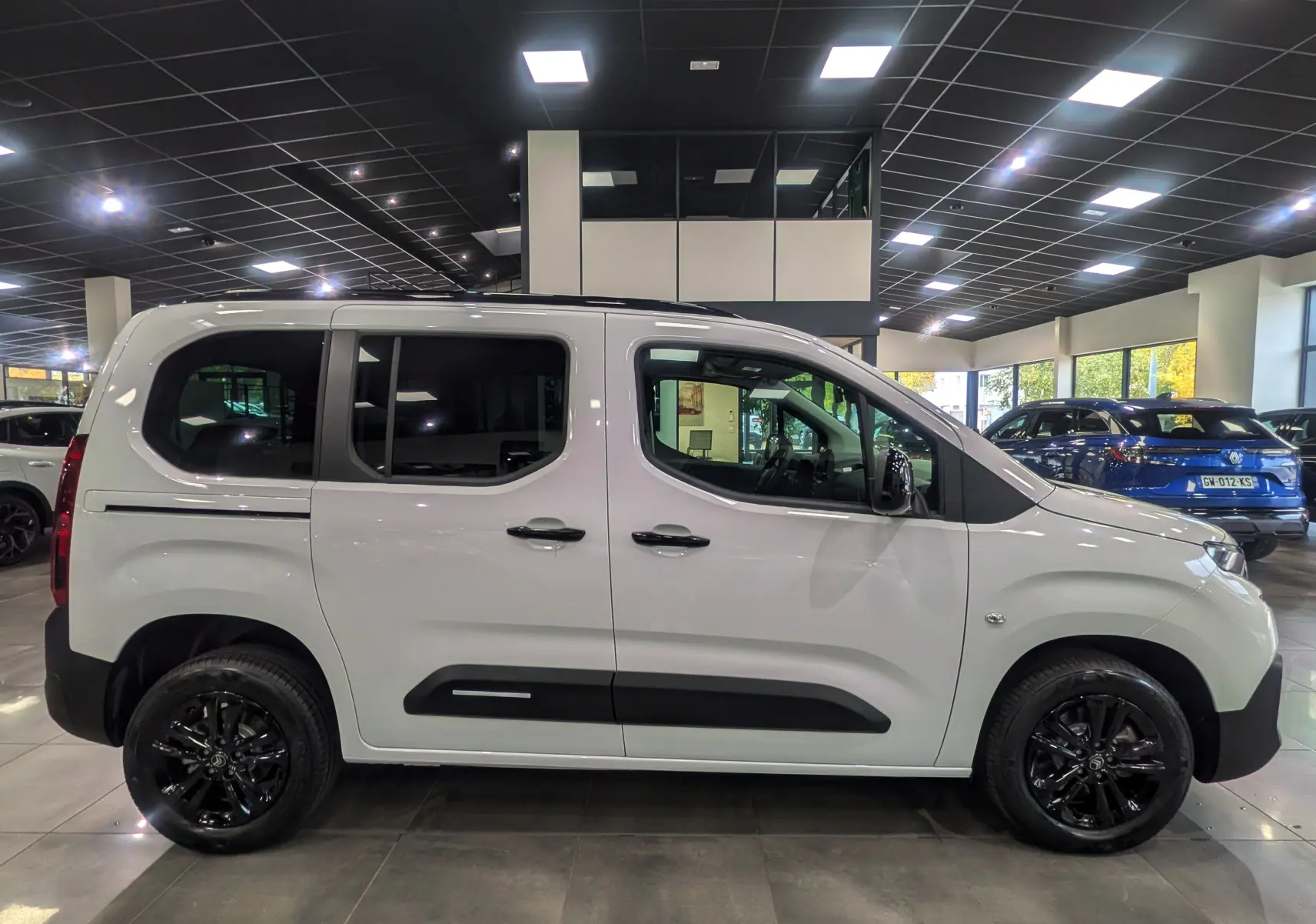 Profil côté gauche d'un Citroën Berlingo blanc Glacier 2025 avec jantes noires et vitres teintées en showroom.