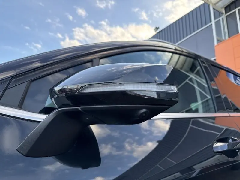 Gros plan sur le rétroviseur droit noir Basalte métallisé du Kia Sportage 2022, reflet du ciel et bâtiment en arrière-plan.