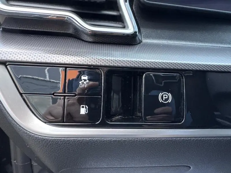 Gros plan sur les boutons noirs de commande du frein à main électrique et de l'antipatinage dans l'habitacle du Kia Sportage noir Basalte.