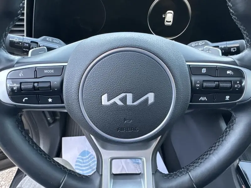Vue rapprochée du volant cuir multifonction noir du Kia Sportage 2022 avec logo KIA au centre et commandes intégrées.