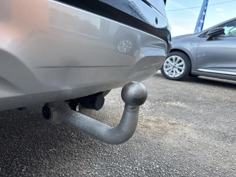 Gros plan sur l'attelage arrière métallique d'un Kia Sportage noir Basalte métallisé, avec une autre voiture grise en arrière-plan.