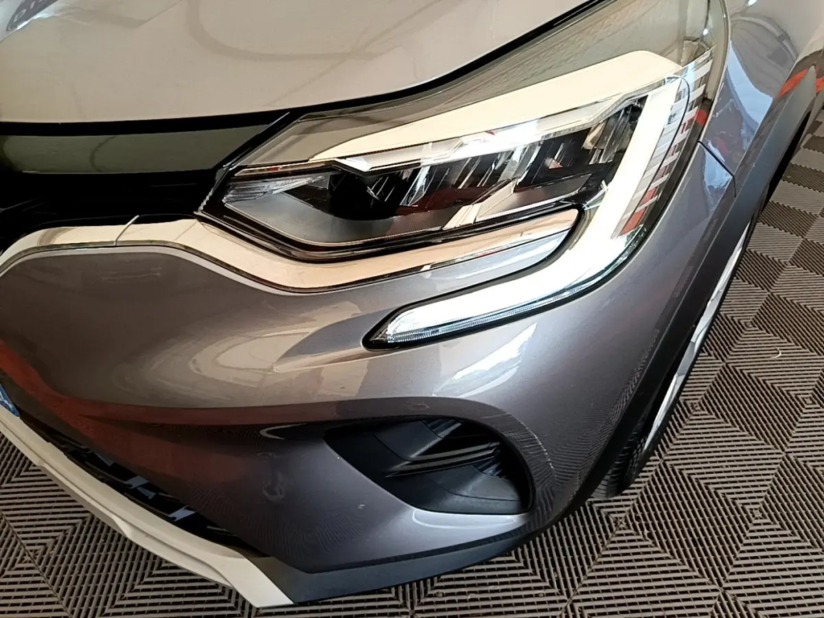 Gros plan sur le phare avant droit du Renault Captur Zen E-Tech hybride gris foncé, avec feux LED et partie de la calandre visible.