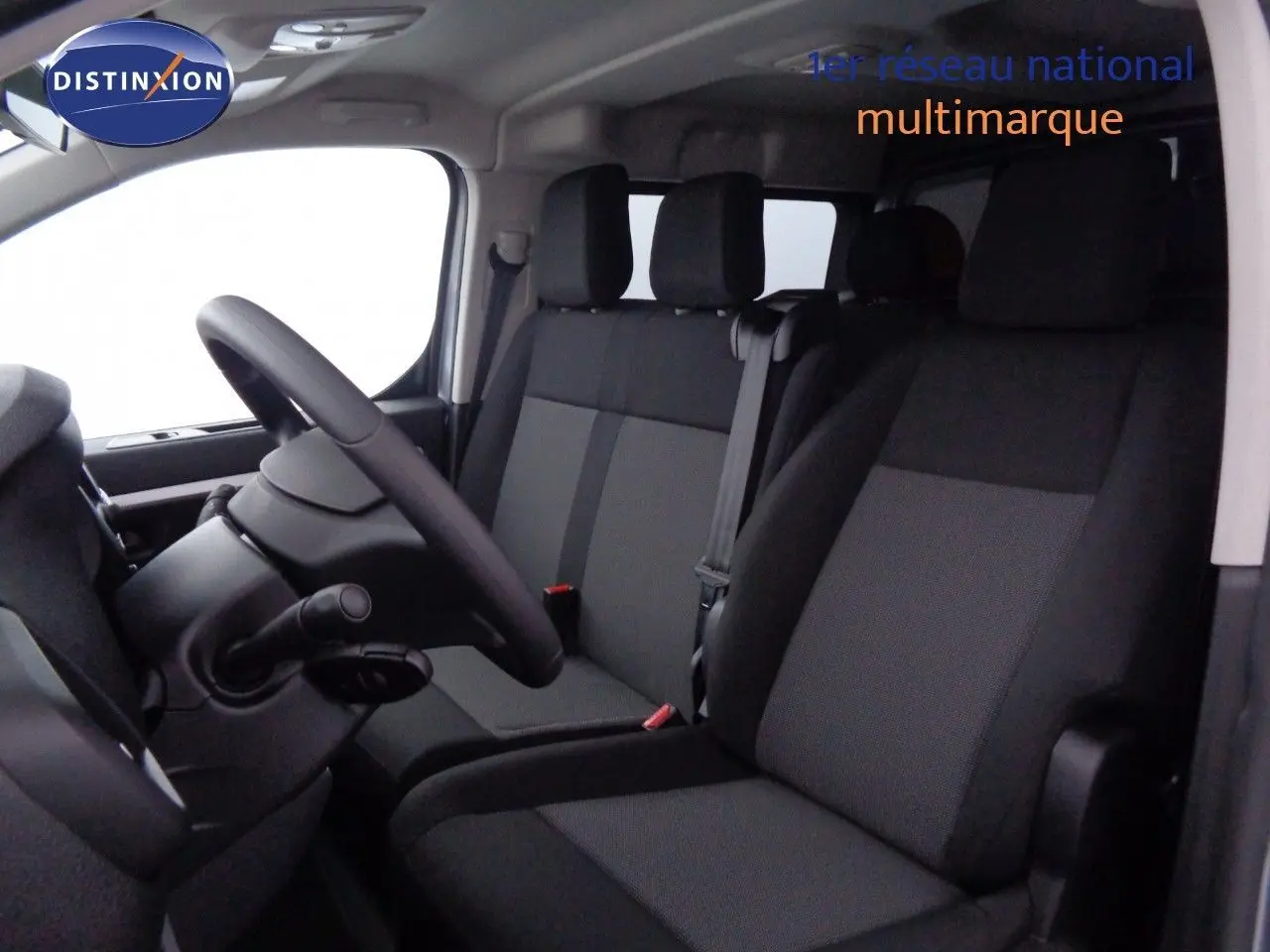 Vue intérieure côté conducteur du Peugeot Expert gris avec sièges tissu gris et noir, volant et ceintures visibles.
