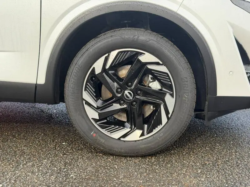 Gros plan sur la roue avant droite du Nissan Qashqai Hybrid e-POWER blanc 2025 avec jante noire et argentée au design moderne.