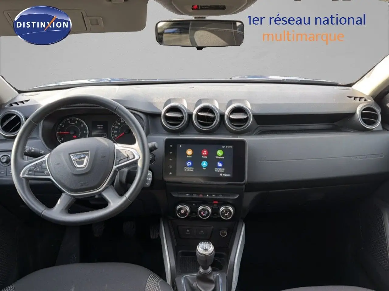 Vue frontale de l'habitacle du Dacia Duster 2022, tableau de bord noir avec écran tactile et volant multifonction.