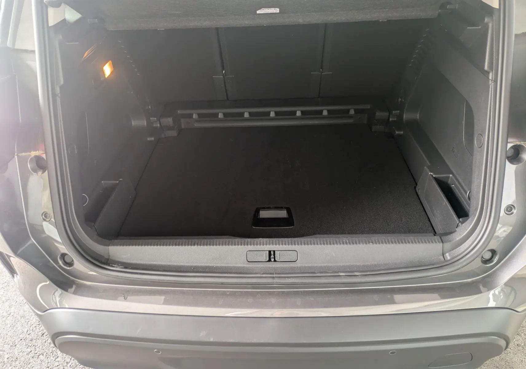 Coffre ouvert vu de l'arrière d'un Citroën C5 Aircross hybride gris platinium, espace de chargement vide et éclairage intérieur allumé.
