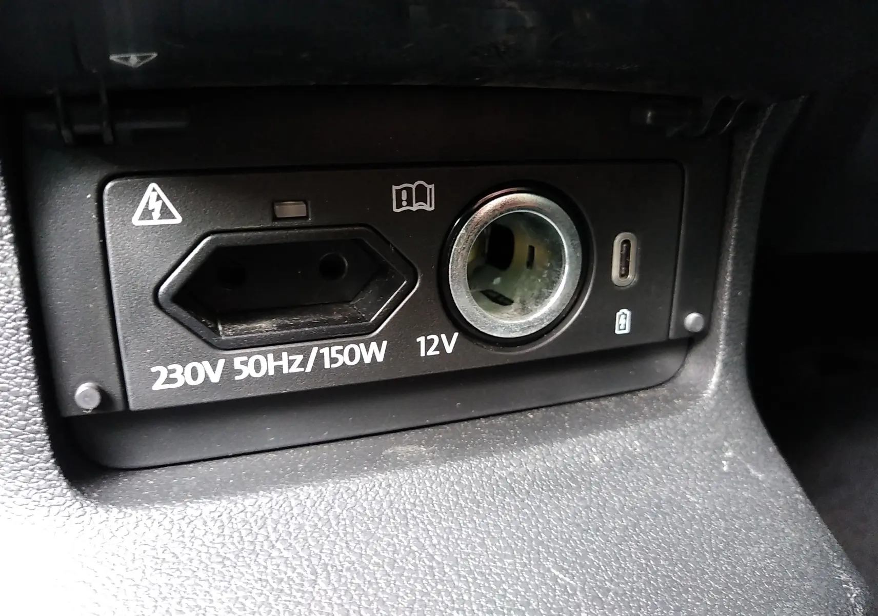 Gros plan sur la prise 230V et l'allume-cigare 12V du tableau de bord intérieur d'un Skoda Karoq gris.