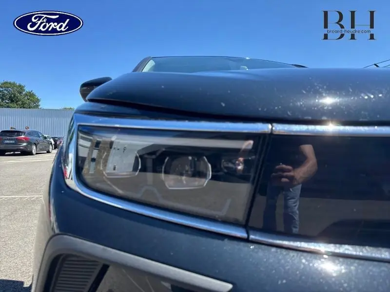 Gros plan sur le phare avant gauche d'un Opel Grandland noir diamant métallisé sous un ciel bleu clair.