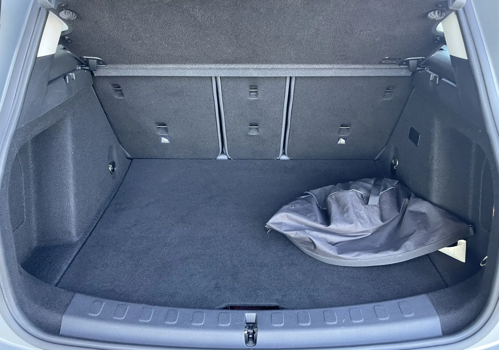 Coffre ouvert d'un MINI Countryman F60 hybride rechargeable gris Moonwalk, montrant un sac noir posé à droite.