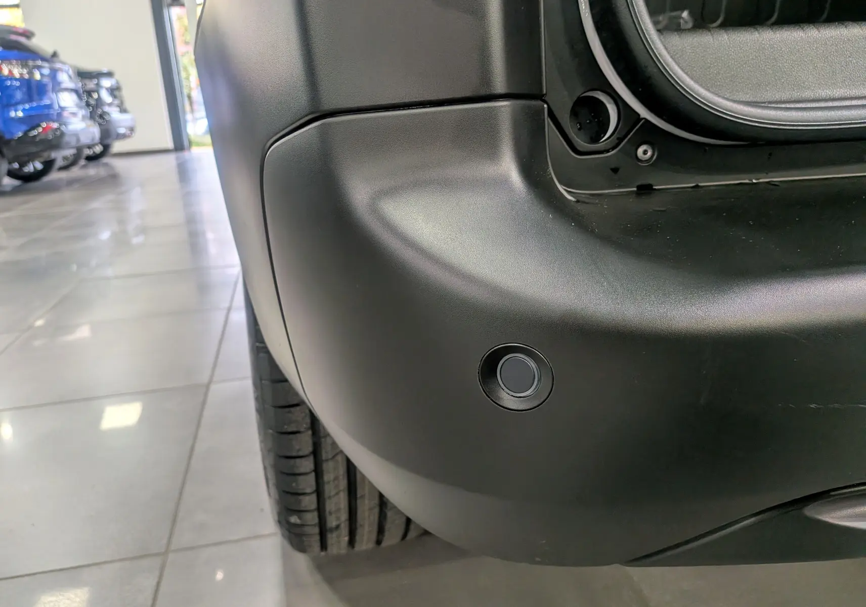 Gros plan sur le pare-chocs arrière noir mat du Citroën Berlingo blanc Glacier, montrant un capteur de stationnement rond.