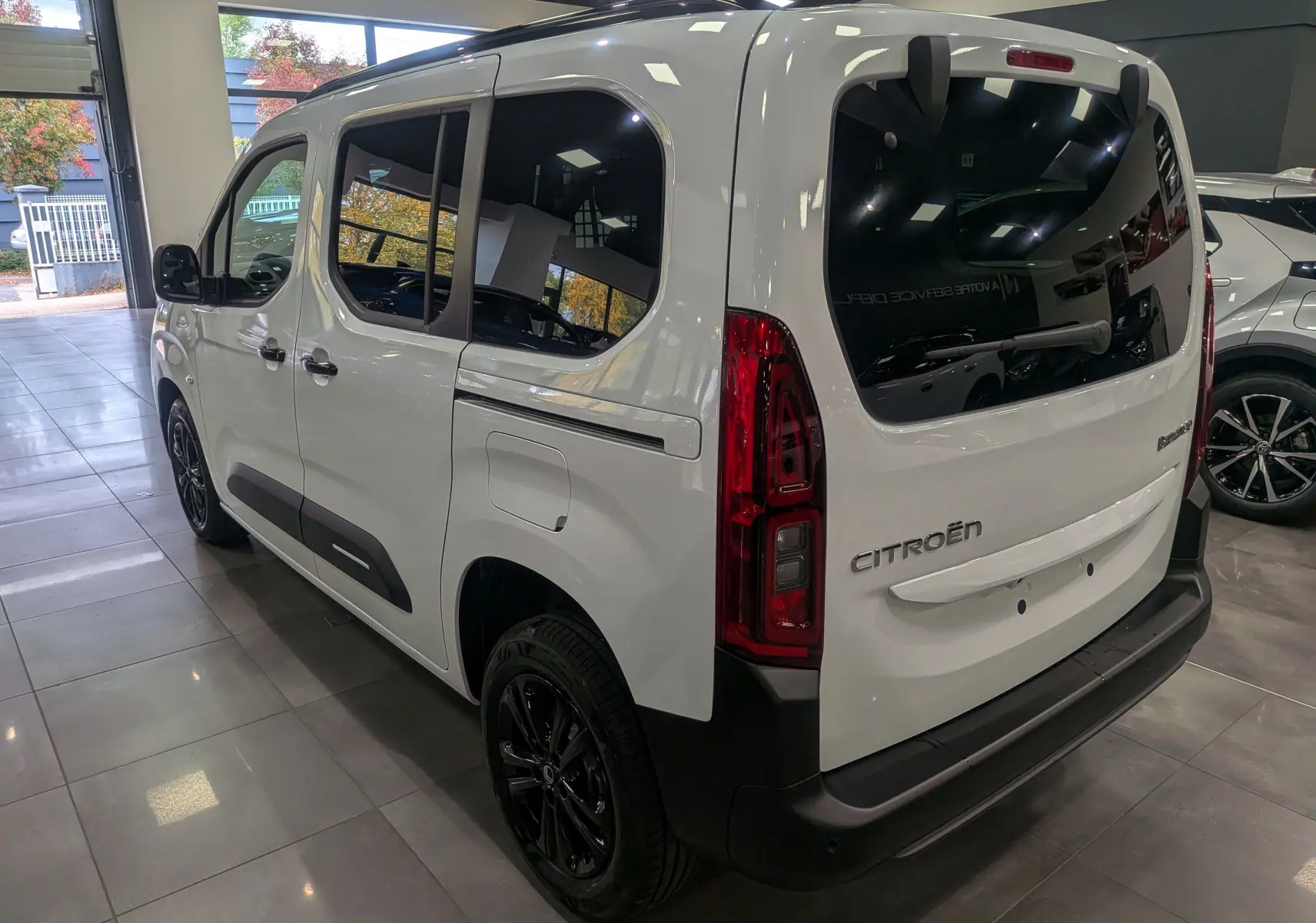 Vue 3/4 arrière droite du Citroën Berlingo blanc Glacier 2025 avec jantes noires et vitres teintées en showroom.