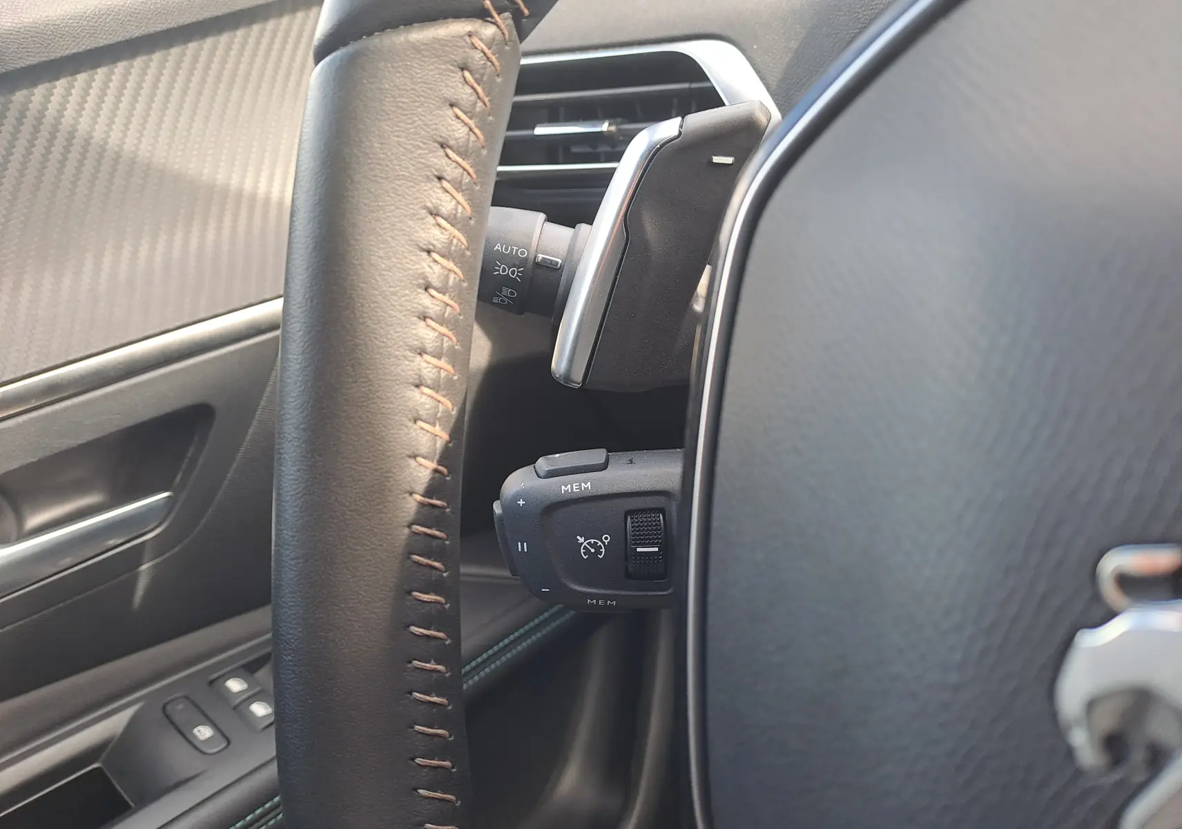 Gros plan sur le volant en cuir noir avec surpiqûres marron du Peugeot 3008 gris platinium, montrant les commandes de régulateur de vitesse.