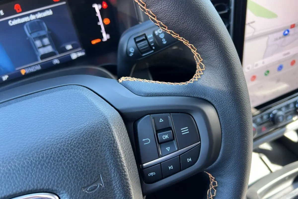 Gros plan sur le volant en cuir noir avec surpiqûres orange du Ford Ranger 2025, affichage numérique et écran tactile visibles.