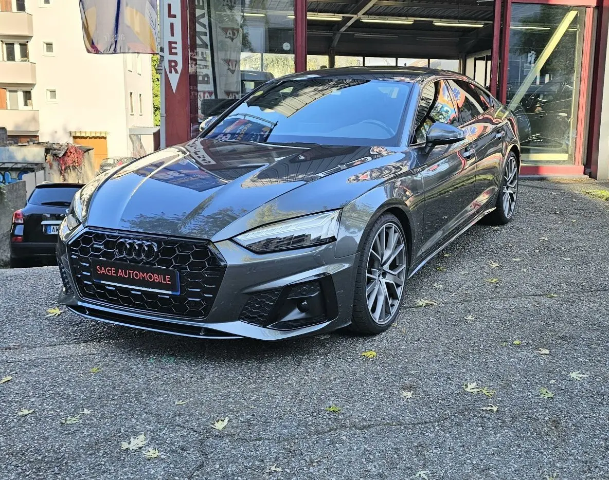 Audi A5 Sportback gris Daytona en 3/4 avant droit, avec calandre hexagonale noire et jantes alliage distinctives.