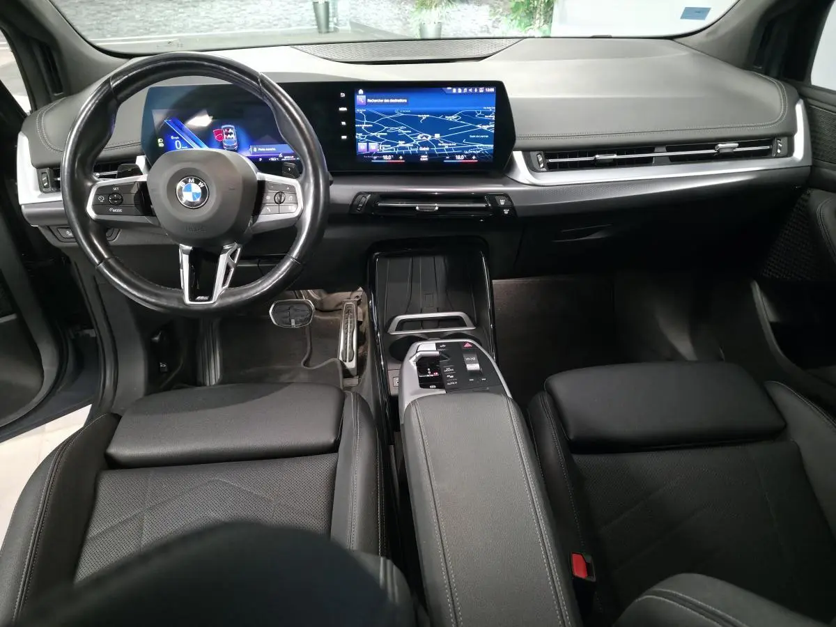 Intérieur noir de la BMW Série 2 218i Active Tourer 2023, vue du tableau de bord avec écran tactile incurvé et volant M cuir.
