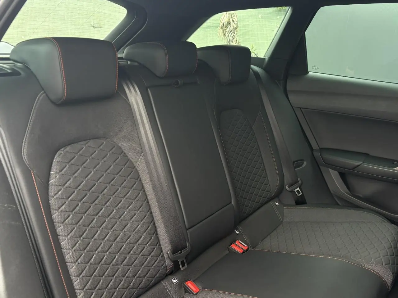 Vue latérale droite de la banquette arrière noire avec surpiqûres rouges et sellerie matelassée du SEAT Leon 2025.